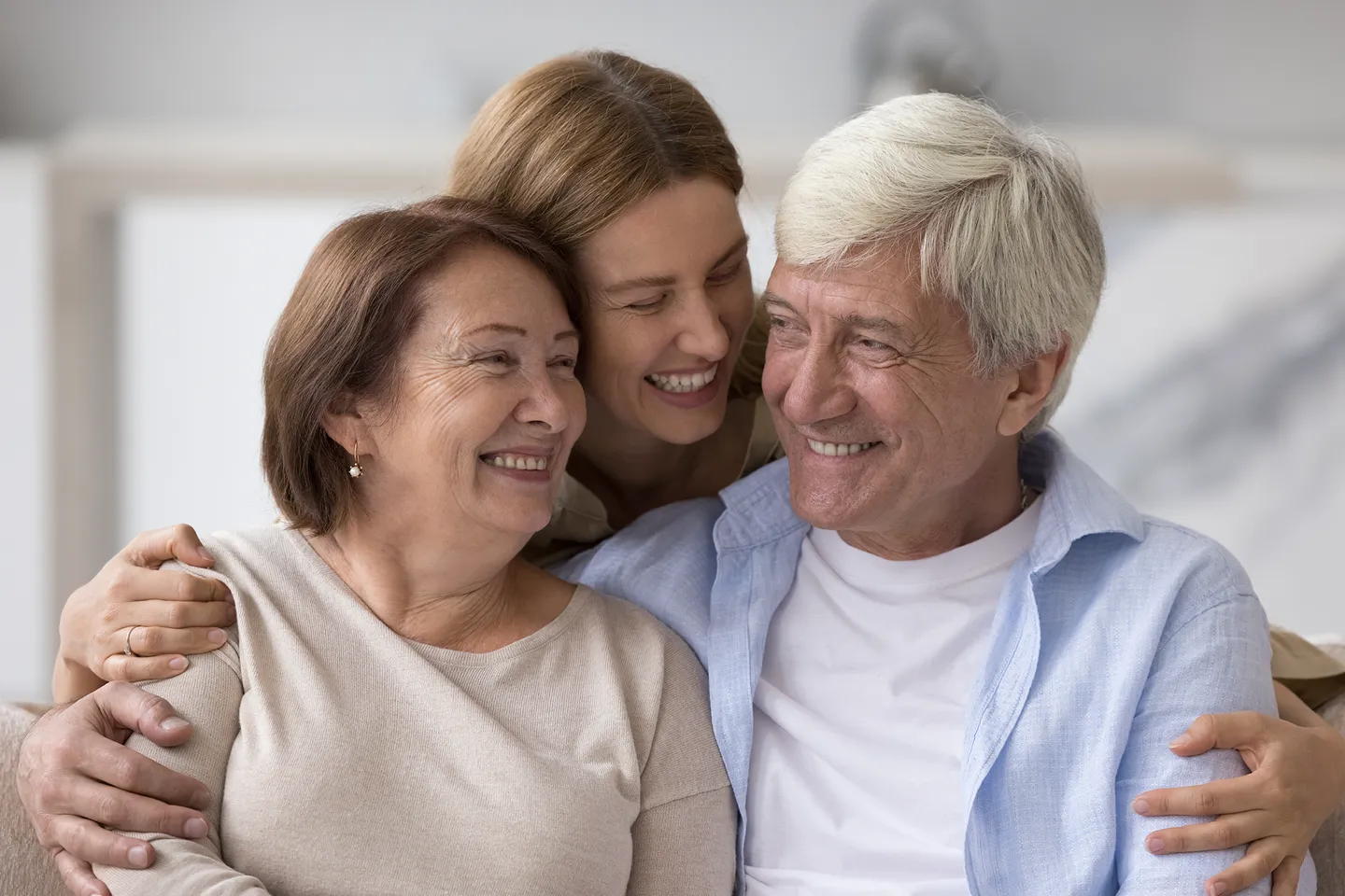 An adult daughter laughing with her mother and father on a couch.