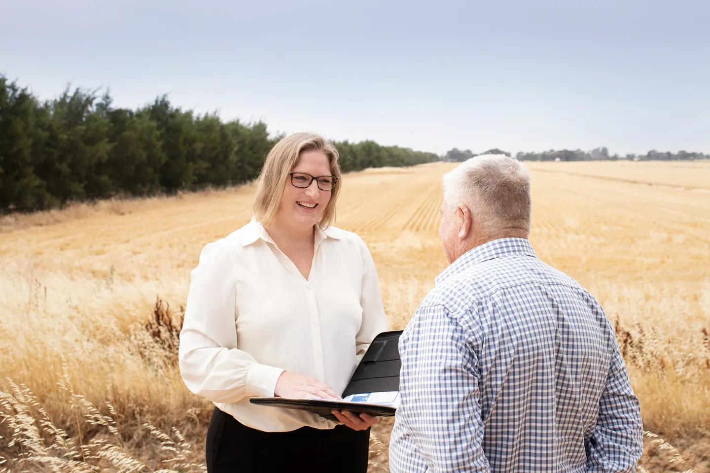 A Beck Legal lawyer and a farmer reading a folder beside a harvested field.